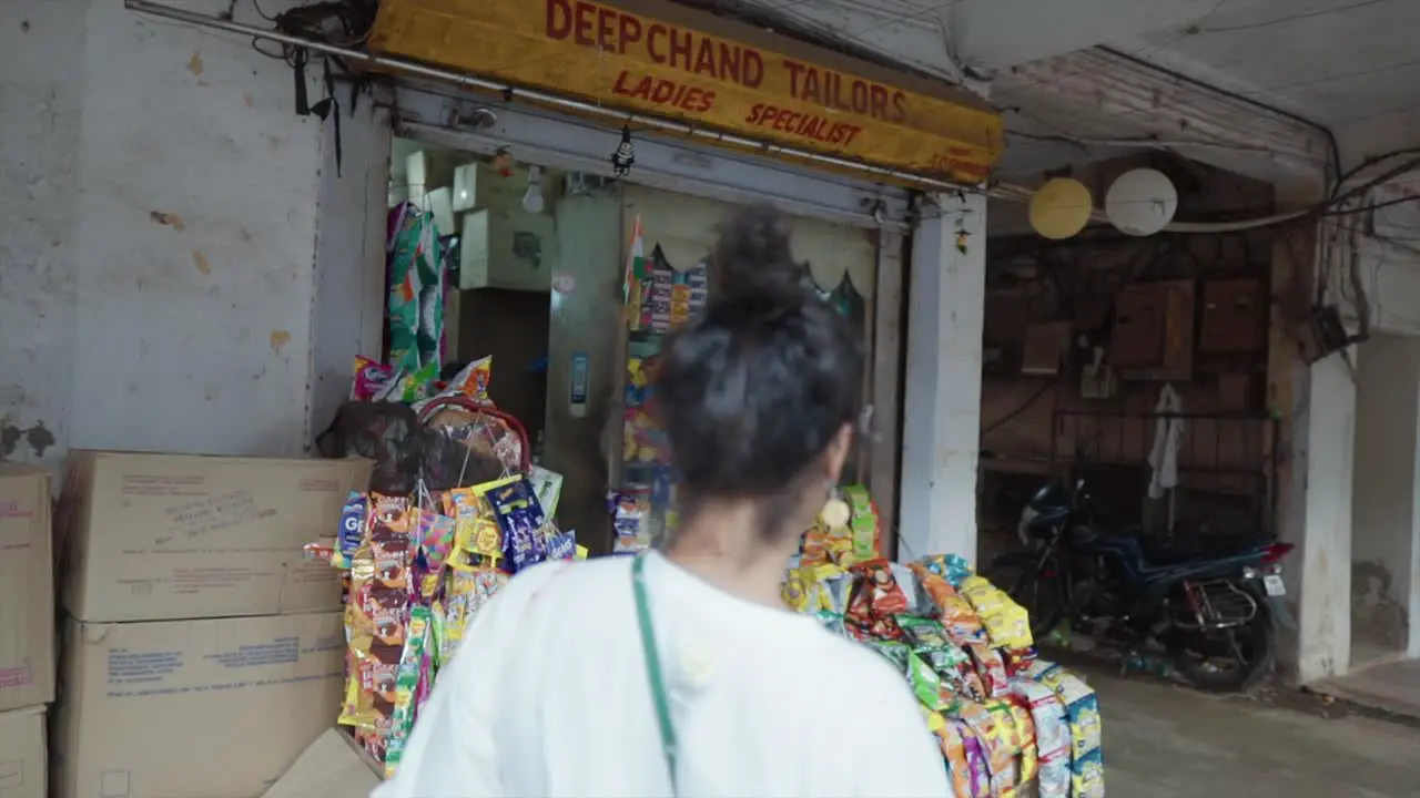 A young woman walking into a shop and looking and shopping for snacks in a street-side shop displaying a variety of snacks outside the store