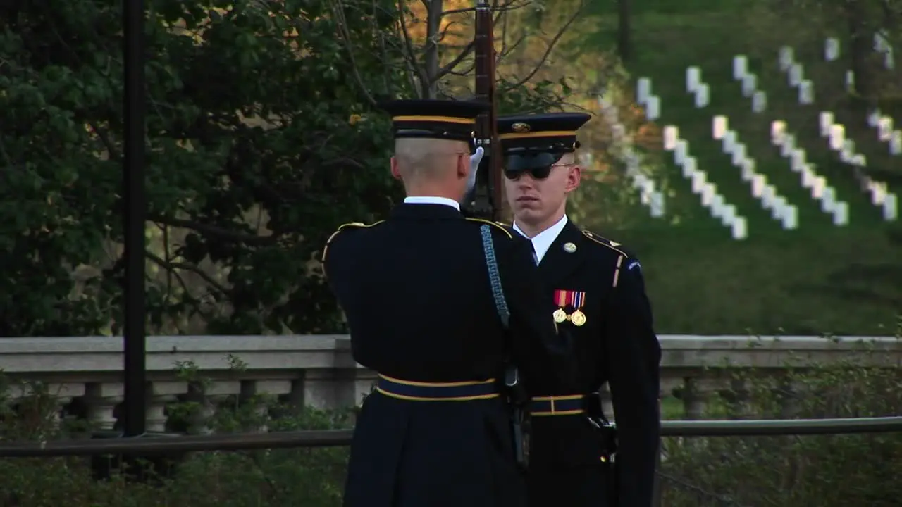 A Soldier Stands At Attention In Full Uniform As Another Soldier Inspects His Gun