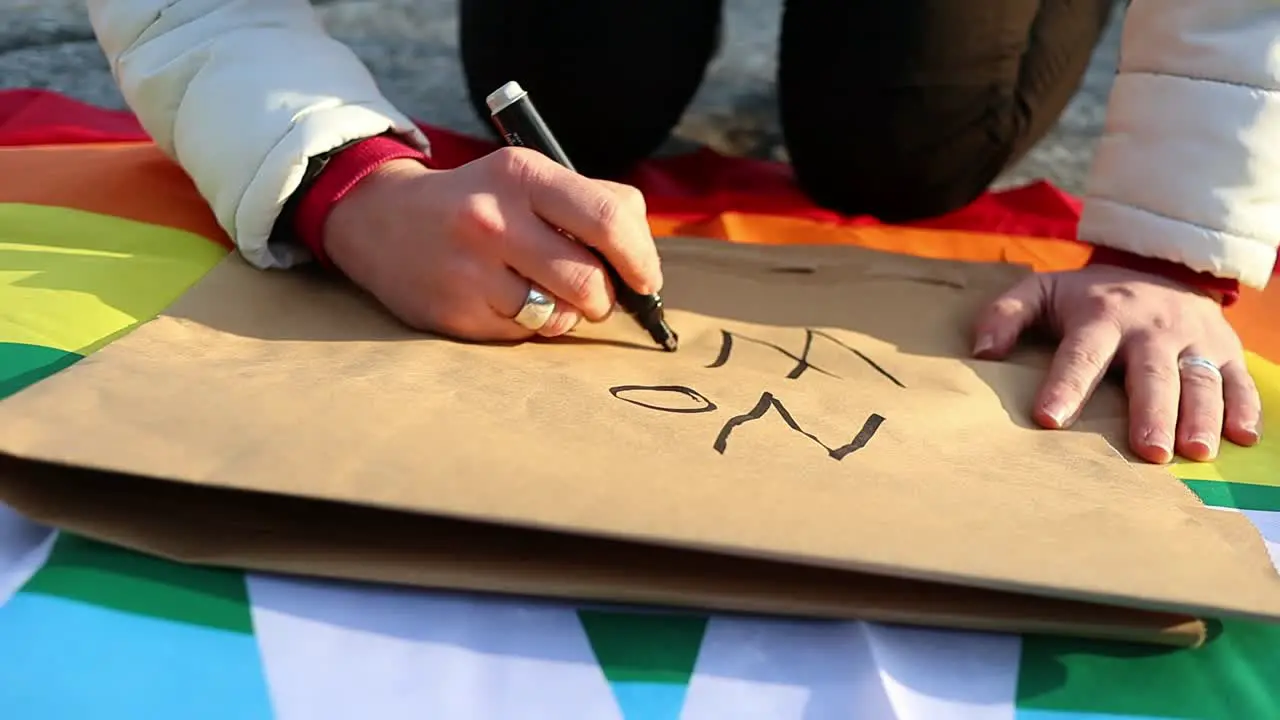 Female caucasian hand writes anti-war protest placard slow motion close up shot