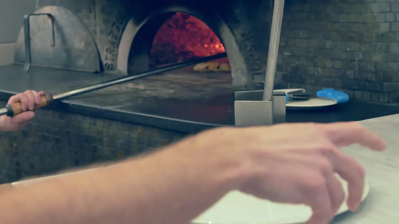 Cook taking pizza out of the oven and placing it on a plate