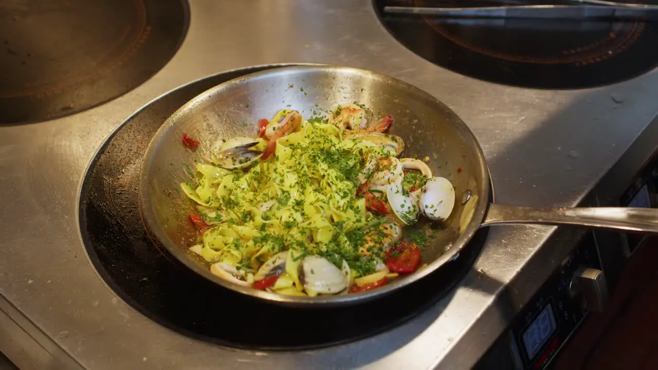 Spaghetti o tagliatelle with seafood preparation in professional restaurant kitchen chef add green Persley before plate