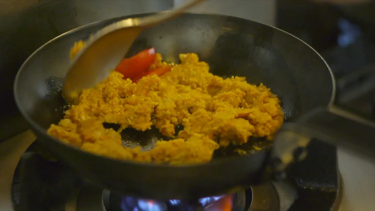 Couscous being stir fried in frying pan with spoon on gas fire stove filmed in close up