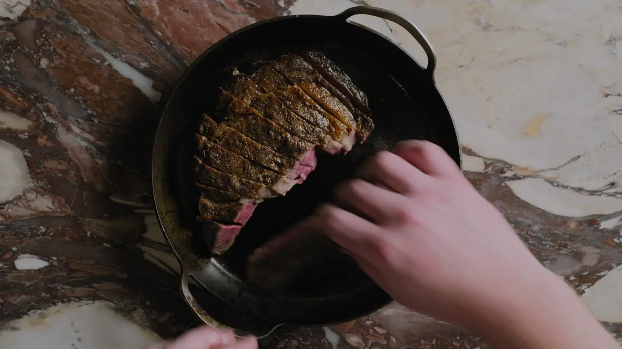 Top-down shot of a ribeye steak being plated into a cast iron pan