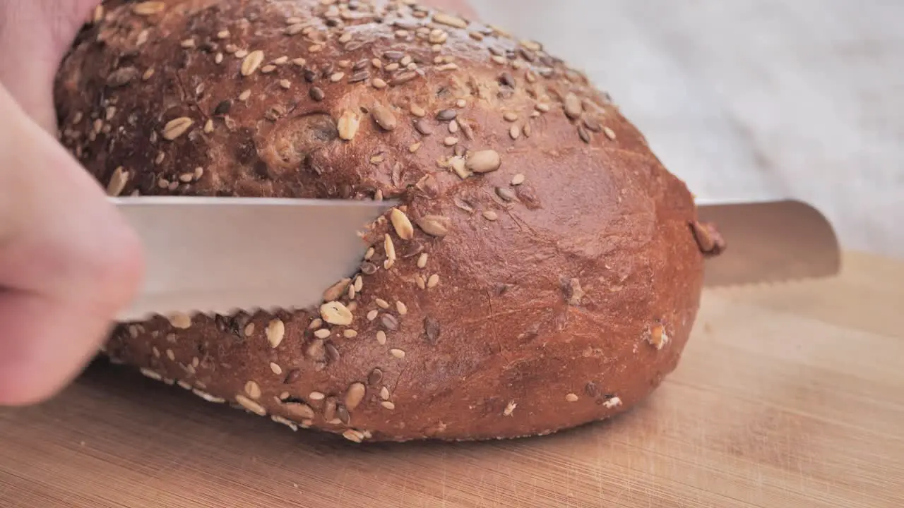 A man cuts freshly baked bread covered with seeds with a knife on a wooden board