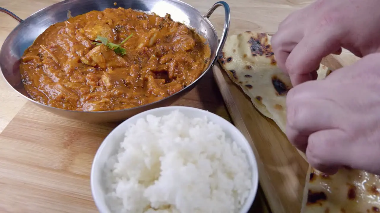 Slider Shot of Tearing off a Piece of Butter Naan and Dipping it in a Homemade Indian Curry in a Balti Dish with Rice