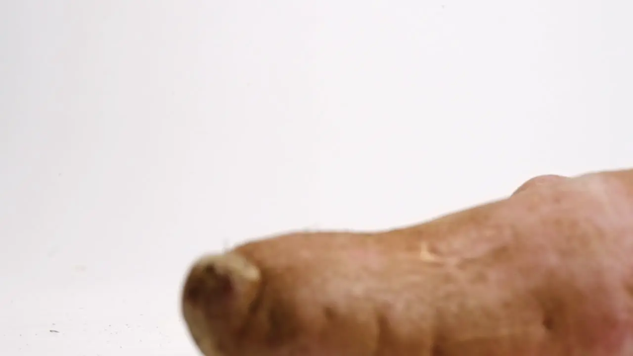 Whole brown sweet potatoes falling onto white backdrop and rolling towards frame in slow motion