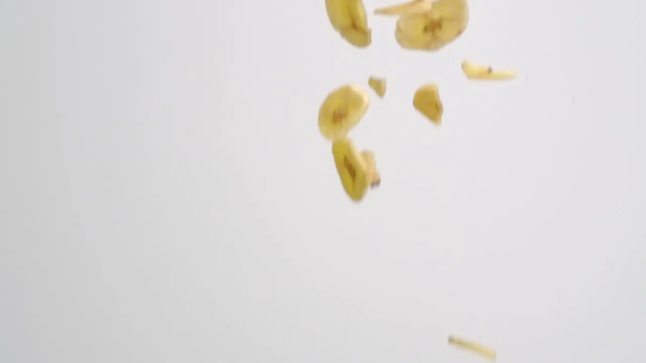 Freeze dried banana slices falling on white backdrop in slow motion