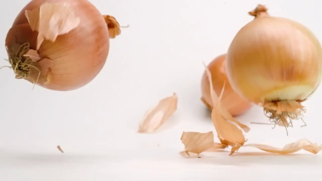 Whole white and yellow sweet onions with skin on falling and bouncing off each other on white table top in slow motion