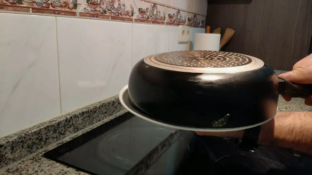 the hands of the cook using a plate to turn the Spanish potato and egg omelette in the pan and finish cooking in electric hob cooker Shot blocked close-up Galicia Spain