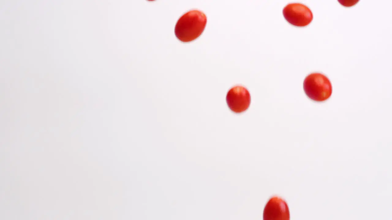 Fresh bright red cherry tomato fruits and vegetables raining down on white backdrop in slow motion