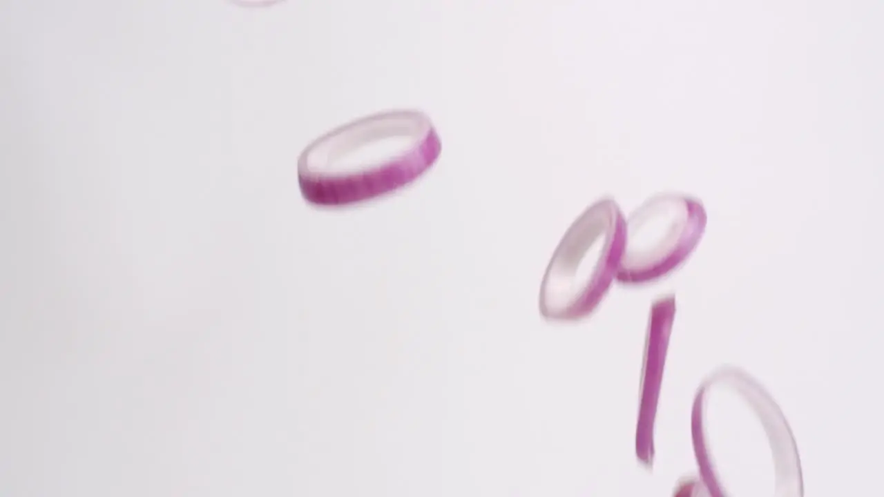 Bright purple fresh red onion rings raining down on white backdrop in slow motion