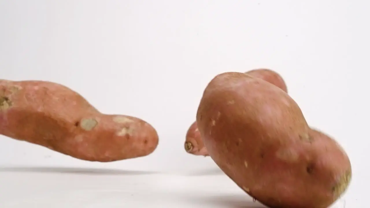 Whole sweet potato root vegetable pieces falling and bouncing on white table top in slow motion