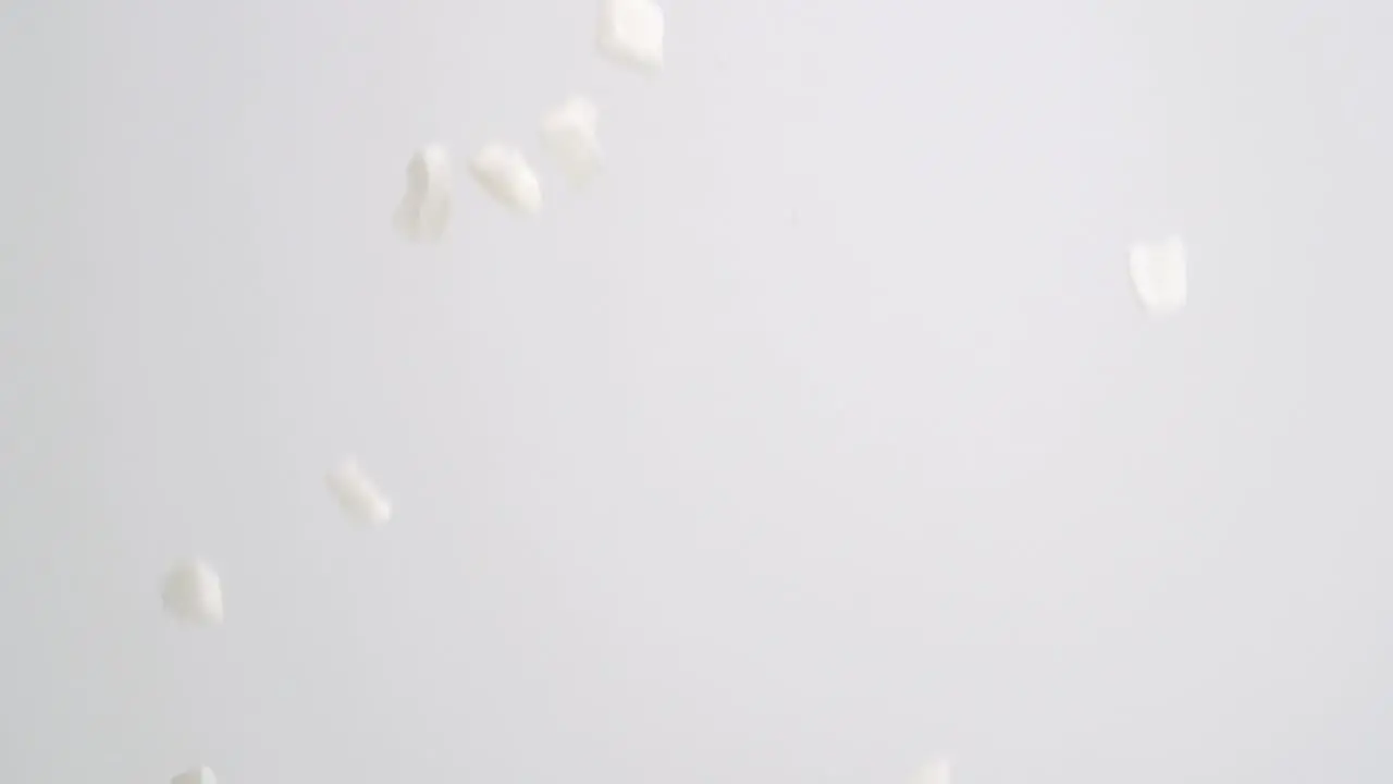 White freeze dried coconut chunks raining down on white backdrop in slow motion