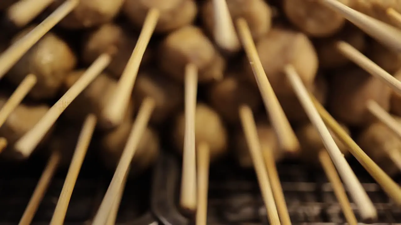 Close-up panning shot of grilled meatball on skewers stacked on hot charcoal grill at street food stall