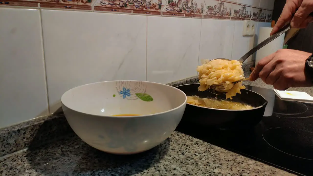 the cook's hands with kitchen utensils remove potatoes cooked in olive oil and mix them with the beaten egg in the bowl cook Spanish omelette in ceramic hob shot blocked close-up Galicia Spain