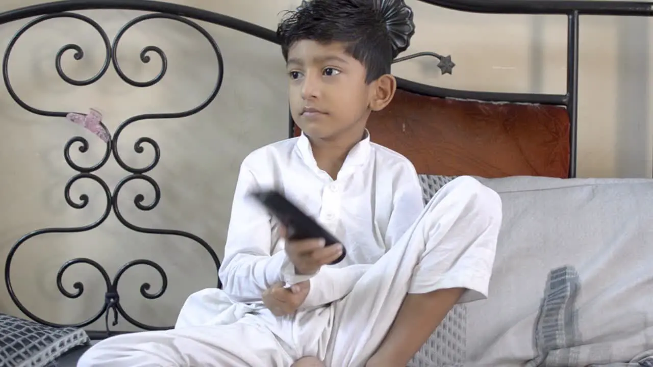 Cute indian asian caucasian boy child changing tv channel with remote and trying to make it work by hitting it front view