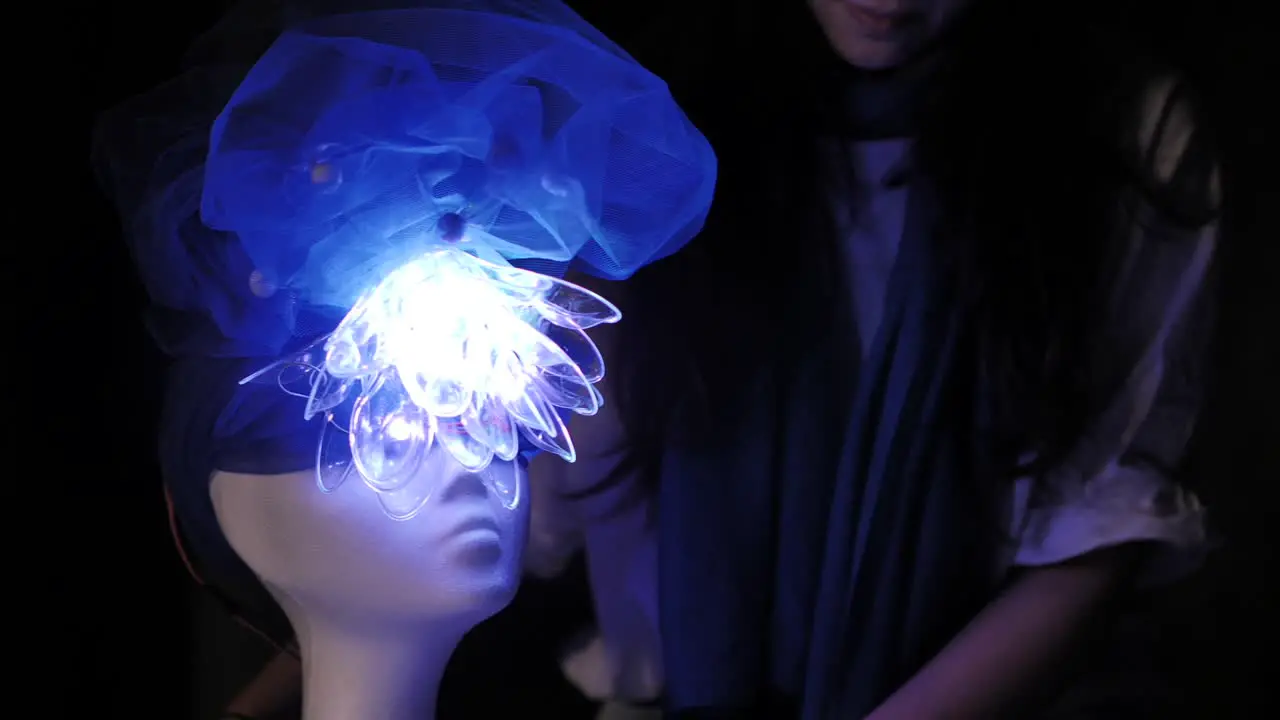 A student working on a weird futuristic manikin head with fluorescent color changing led light flower design hat for a design project