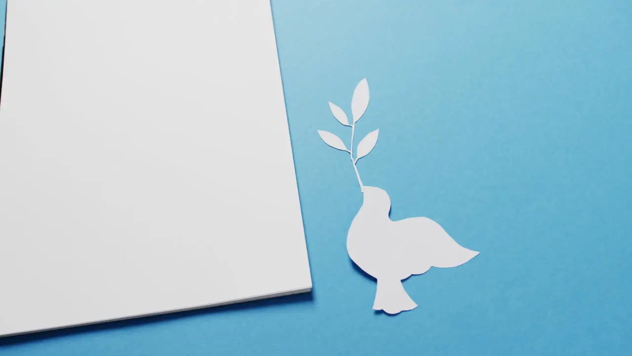 Close up of white dove with leaf white paper and copy space on blue background