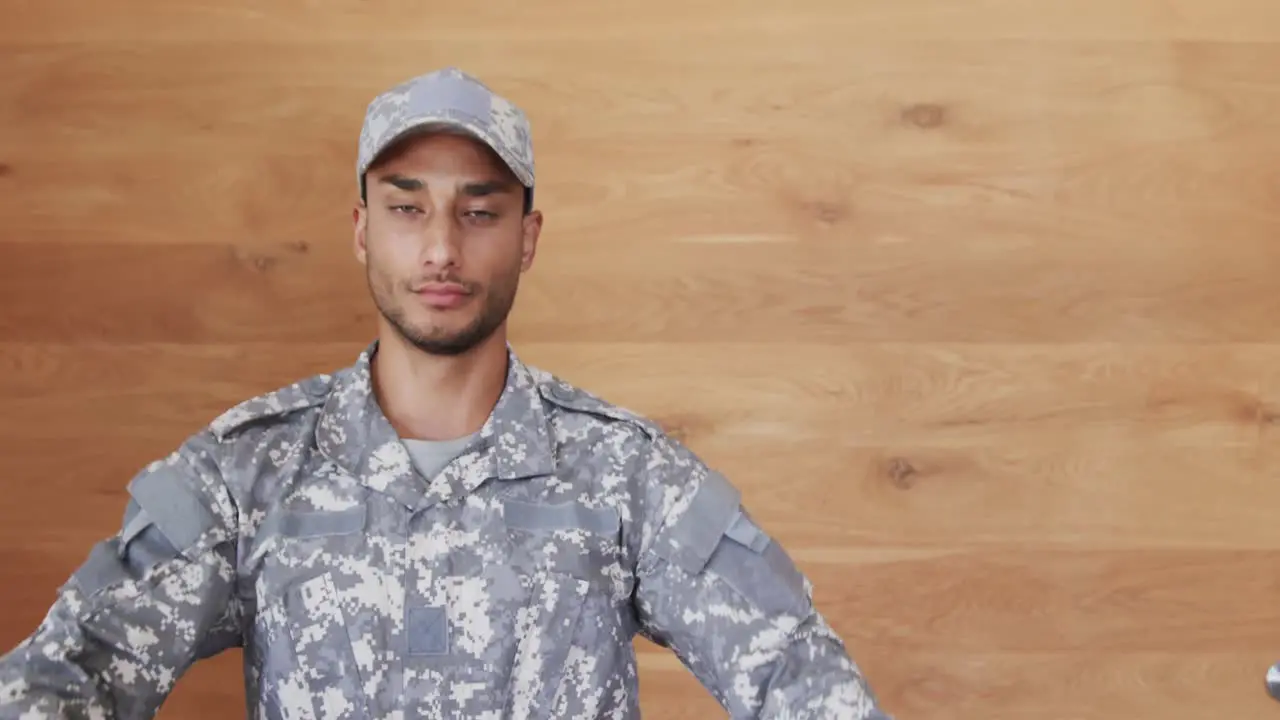 Portrait of biracial male soldier in uniform sitting in front of wooden wall slow motion