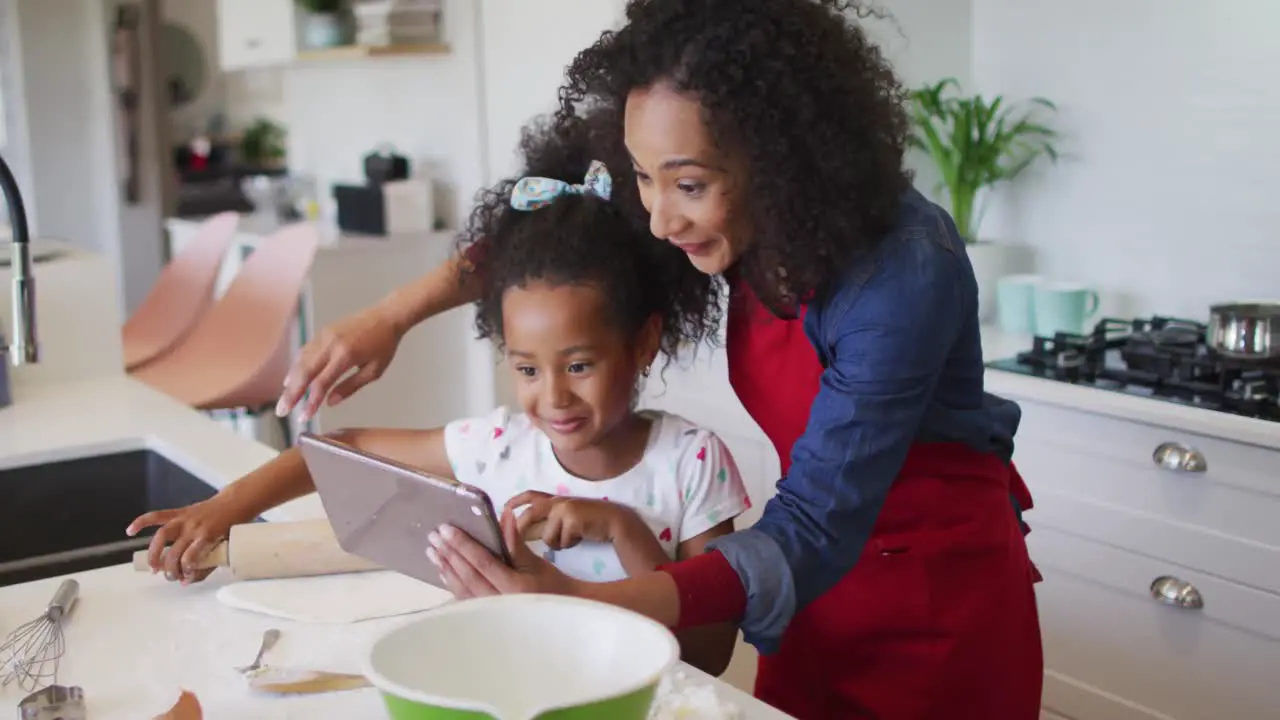 Happy african american mother and daughter using tablet and baking together