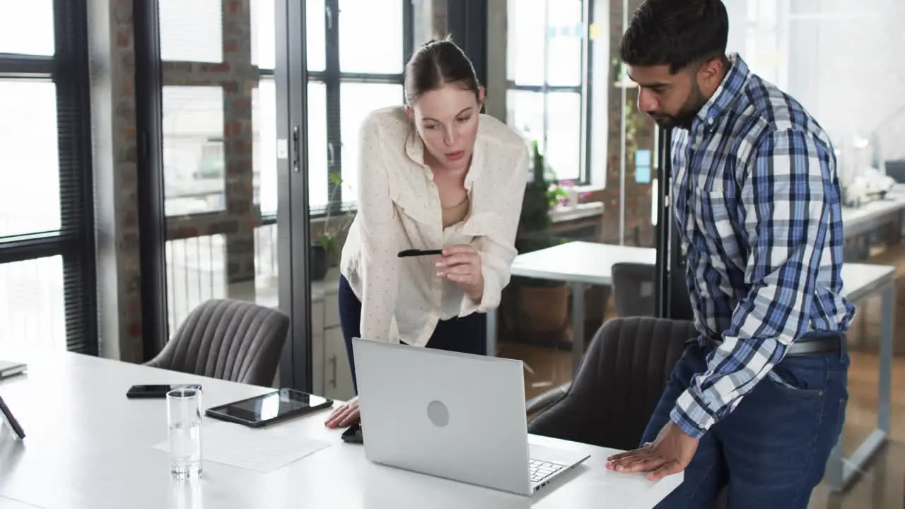 Young Caucasian woman and Asian man review business content on a laptop in an office