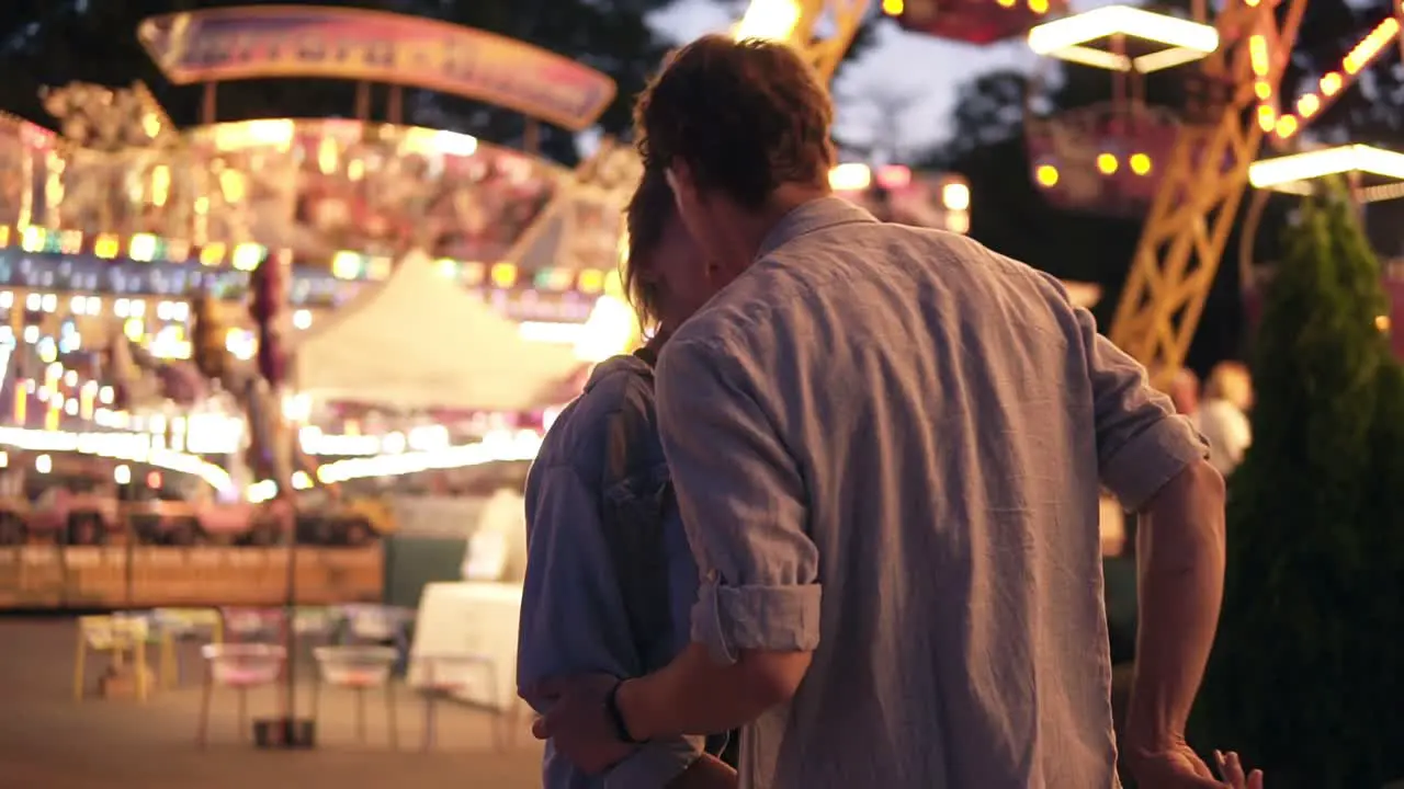 Side Portrait Of An Attractive Young Couple Meeting In An Amusement Park With A Colorful Brightful Sights