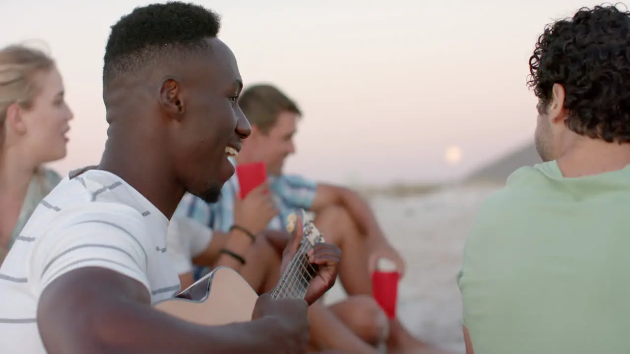 Young African American man plays guitar at a beach gathering at a party