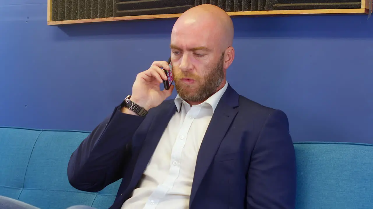 Business man in suit listening to someone on his mobile cell phone while sitting on a sofa couch in home office