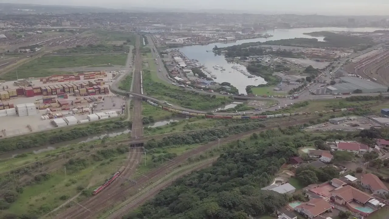 Aerial footage of Durban harbour with yachts and traffic consisting of trucks and moving trains over a highway with cargo container depot in view