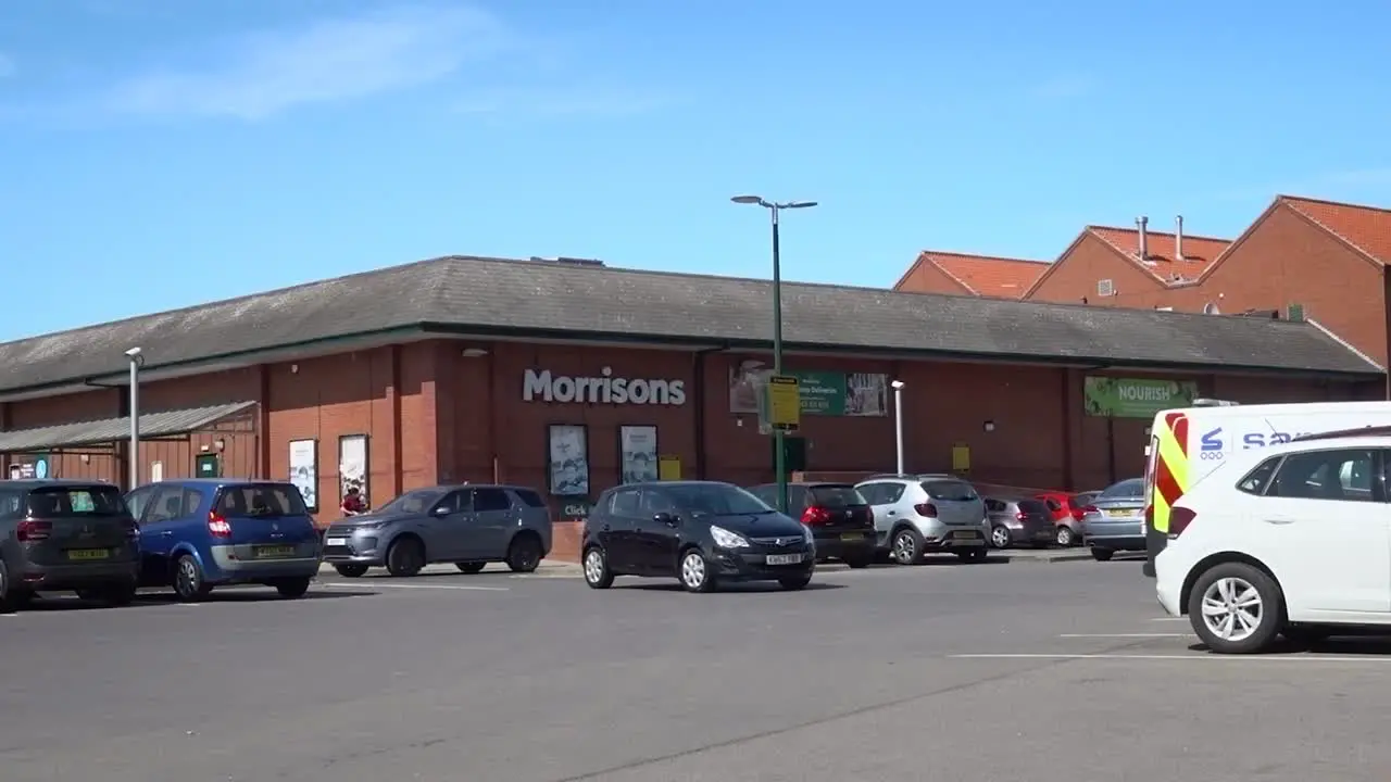 Cars moving and people walking in and out of a modest sized supermarket in England