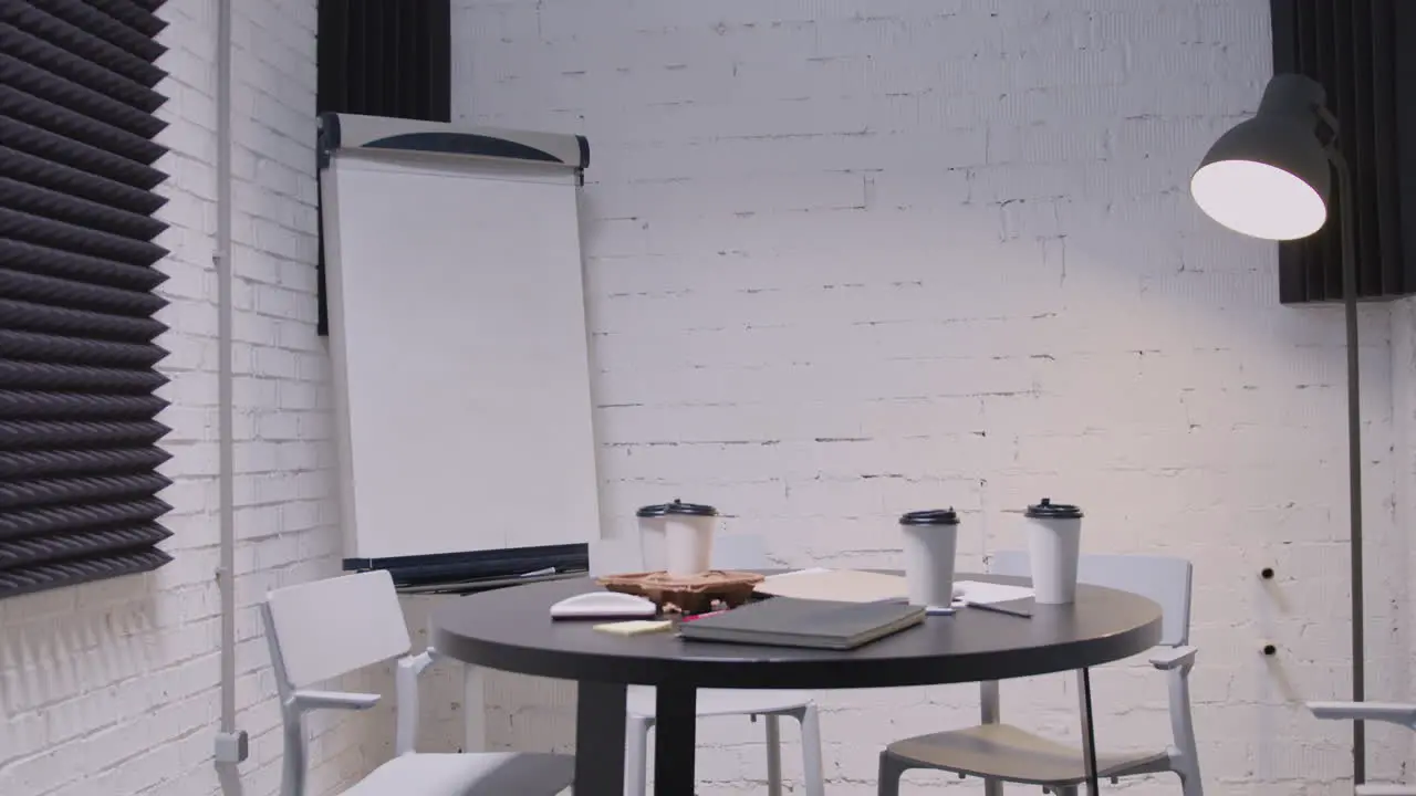 Empty Small Meeting Room With Round Black Table White Chairs Takeaway Coffee Notebooks Floor Lamp And Whiteboard