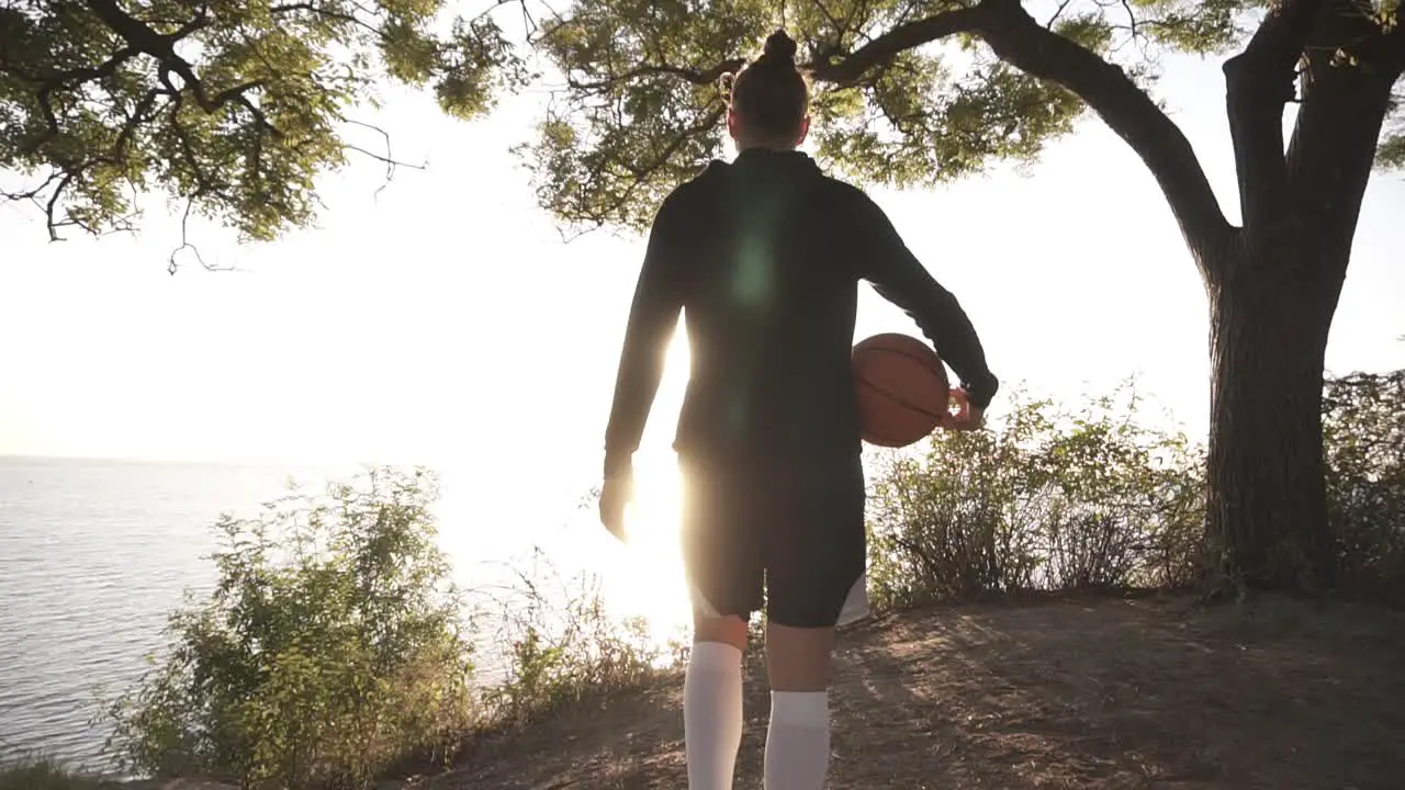 A Basketball Player Girl Comes With A Ball In Her Hand Coming Up To The Slope With Trees Around