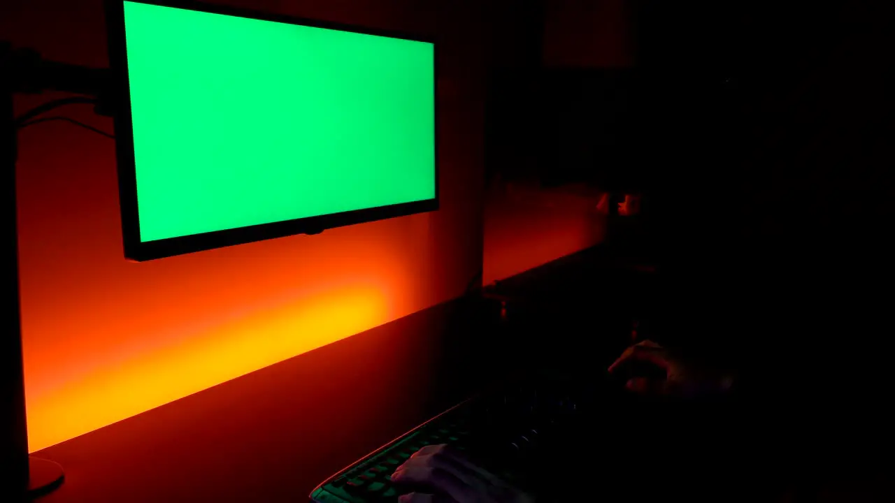 Green screen Caucasian hands on dark keyboard with display monitor above yellow and orange lights