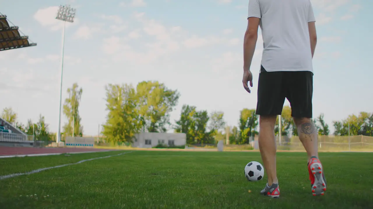 A football player in the stadium goes with the ball on the field hitting the ball with his foot