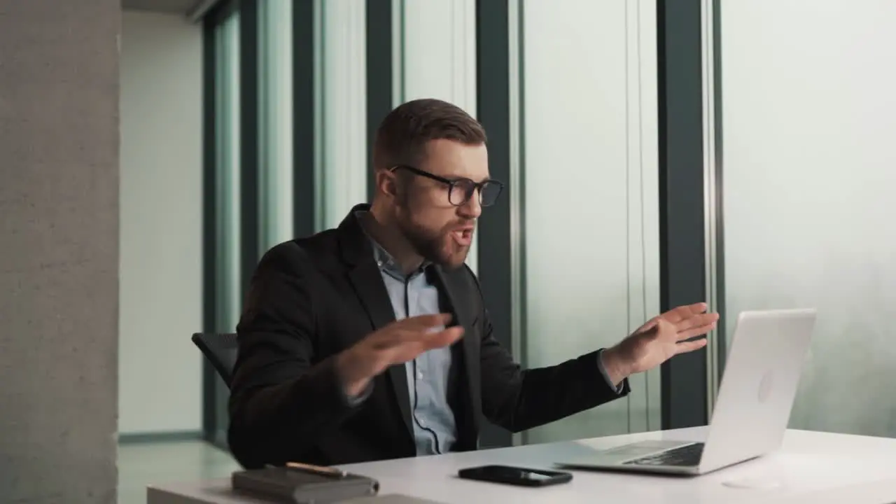 A man in business clothes scolds an employee over a video call while sitting at a laptop