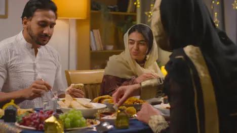 Muslim Muslim Family Sitting Around Table At Home Eating Meal To Celebrate Eid