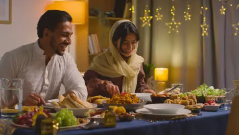 Muslim Muslim Family Sitting Around Table At Home With Woman Serving Biryani At Meal To Celebrate Eid 1