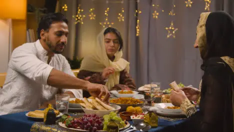 Muslim Family Sitting Around Table At Home Eating Meal To Celebrate Eid