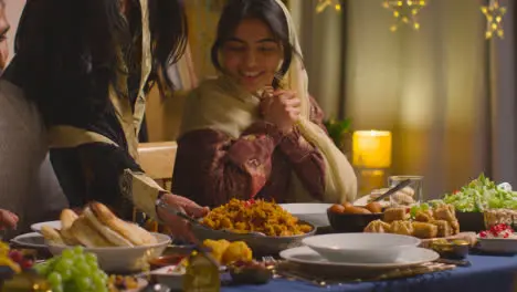 Muslim Muslim Family Sitting Around Table At Home With Woman Serving Biryani At Meal To Celebrate Eid