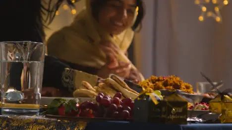 Muslim Family Sitting Around Table With Food For Meal Celebrating Eid Being Served