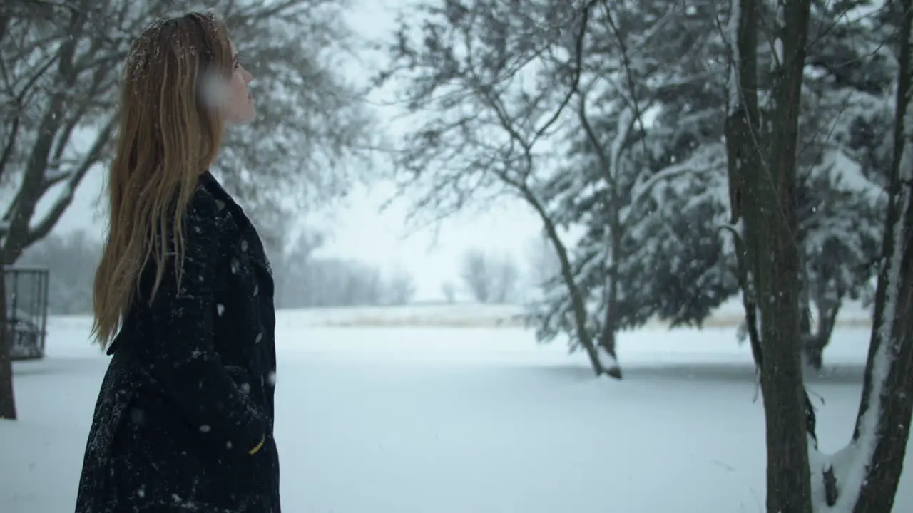 Woman walking outside in slow motion watching Christmas winter snow as snowflakes fall in cinematic slow motion