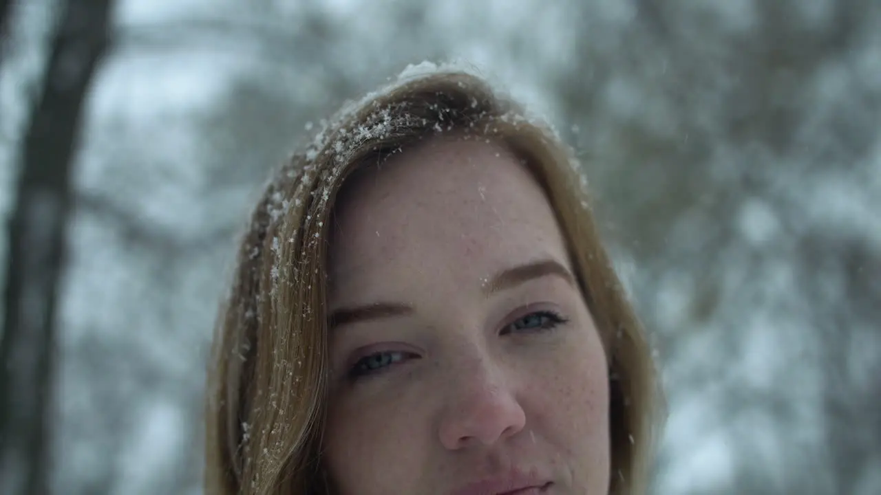 Woman outside in slow motion winter snow looks at camera as snowflakes fall in cinematic slow motion