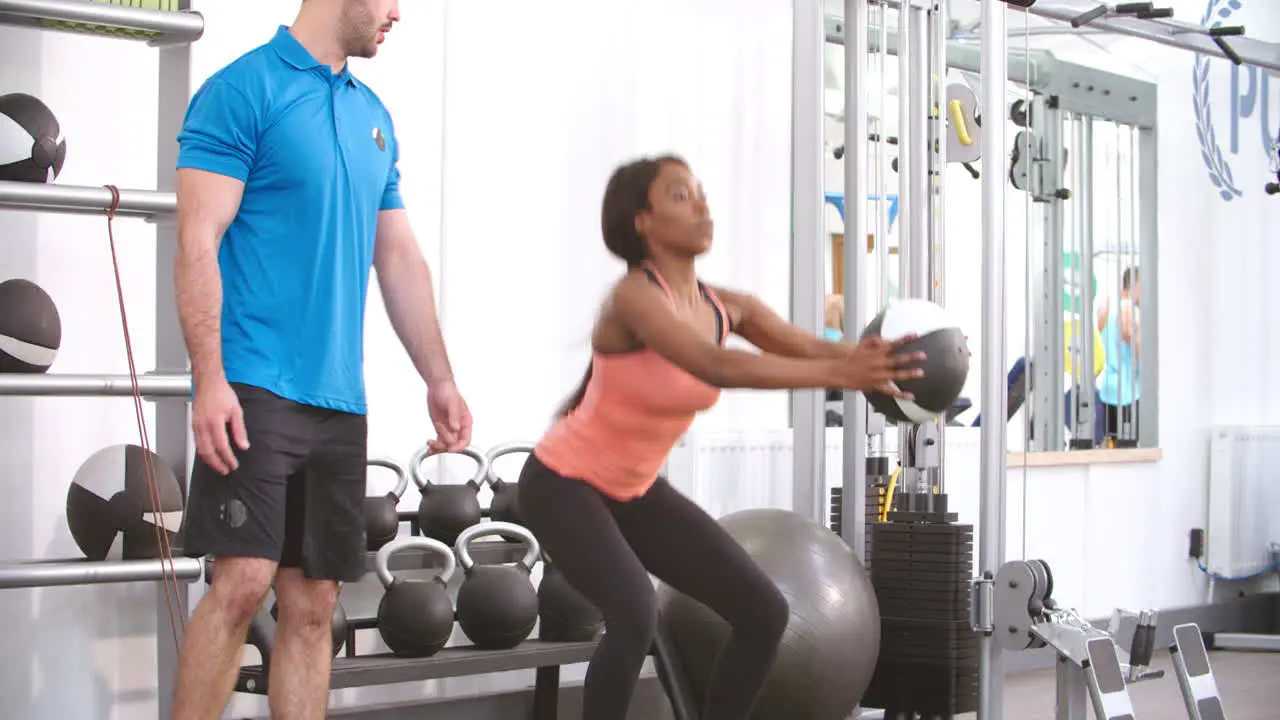 Young woman doing squats in a gym with advice from a trainer