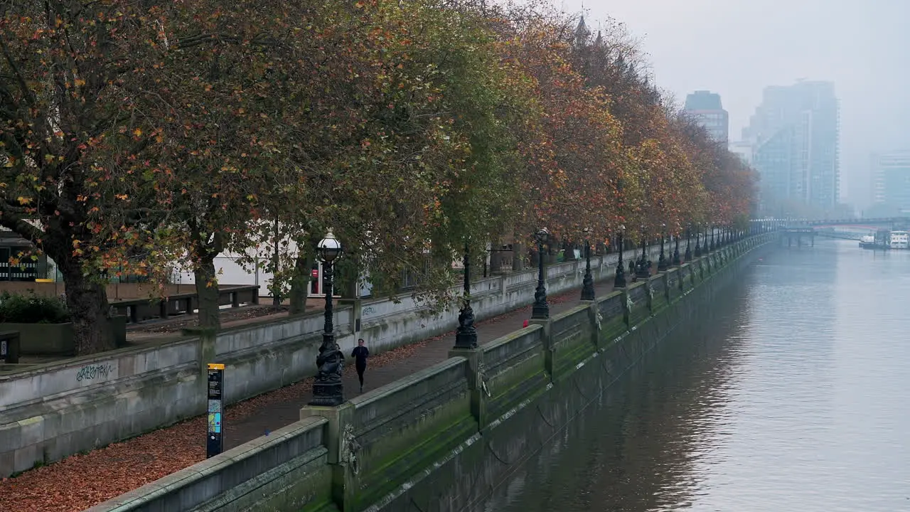 London in Coronavirus Covid-19 lockdown with people running and jogging along River Thames on South Bank with autumn trees on atmospheric misty blue morning in England UK at rush hour