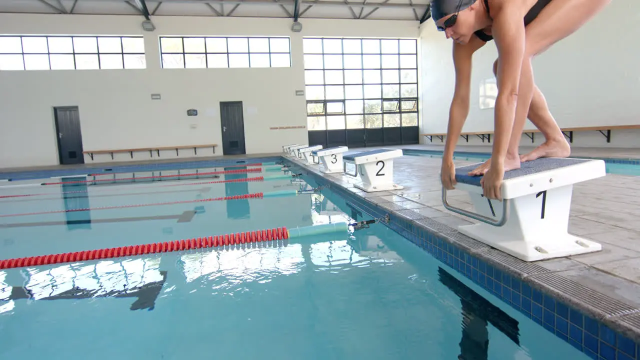 Swimmer poised on starting block at indoor pool