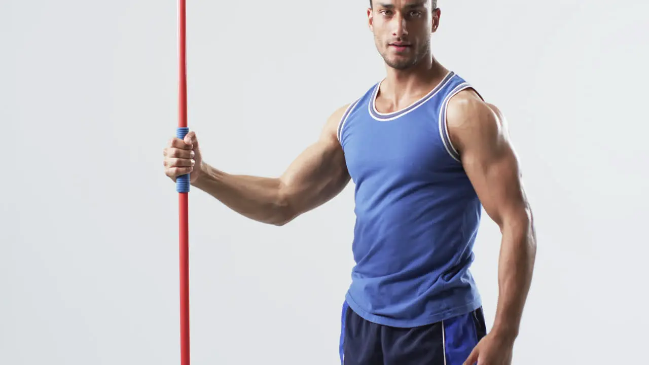 Muscular athlete man holds a javelin at the gym on a white background