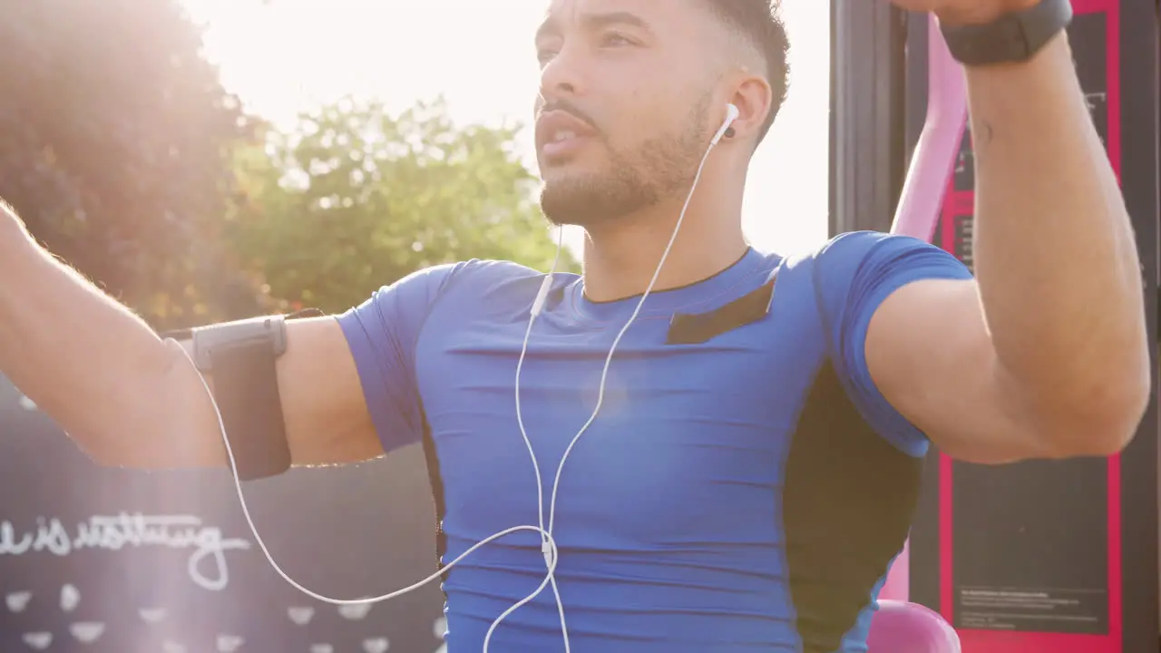 Young male athlete using outdoor gym backlit