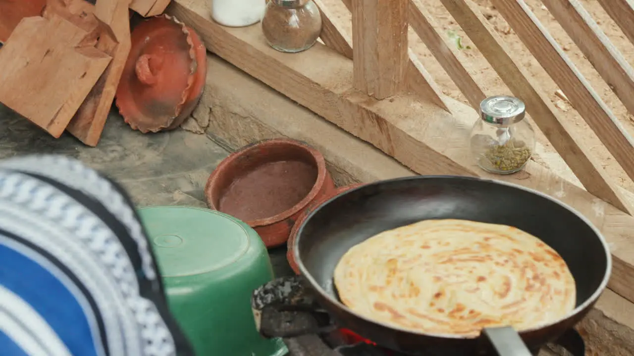 traditional African cooking scene featuring a chapati which is a type of flatbread being cooked on a frying pan over an open flame