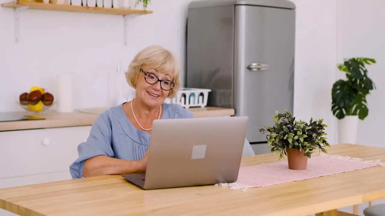 Glückliche Seniorin Die Am Tisch In Der Küche Sitzt Und über Videoanruf Auf Einem Modernen Laptop Spricht