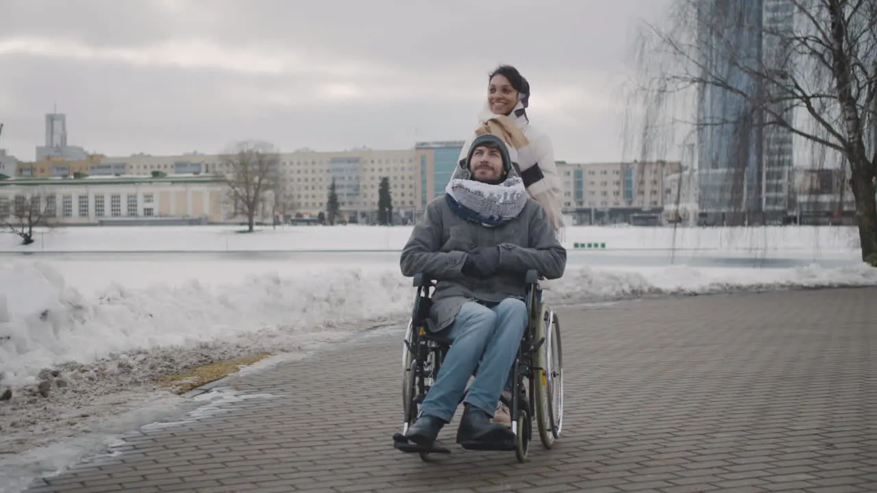 Happy Muslim Woman Taking Her Disabled Friend In Wheelchair On A Walk Around The City In Winter